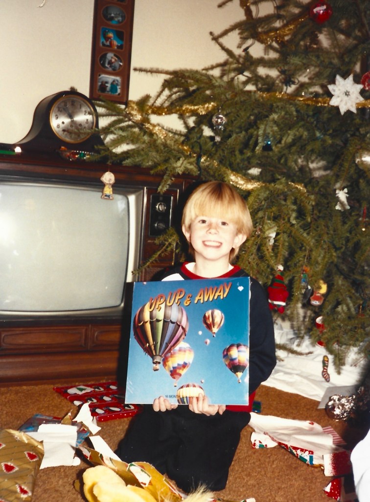 Young boy holding an opened christmas gift that is a hot air balloon calenadar titled "Up Up and Away"